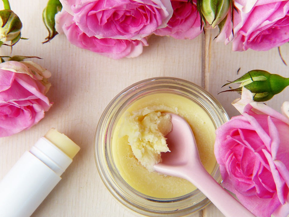 Pot of Vegan Lip Balm and lip balm stick surrounded randomly by roses 