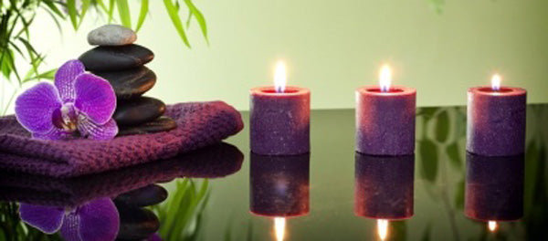 Candle supplies showing 3 lit candles near a towel with rocks and an orchid