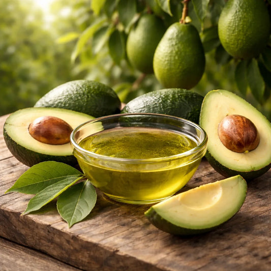 Avocado oil in a glass bowl with whole and sliced avocados on a wooden surface.
