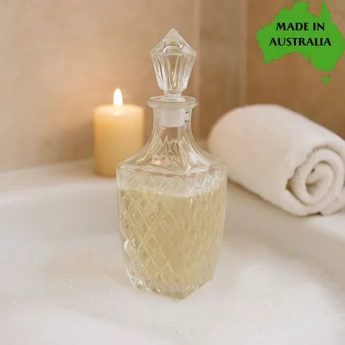 Clear glass decanter filled with bubble bath with a candle and towel on a neutral background, featuring 'Made in Australia' label.