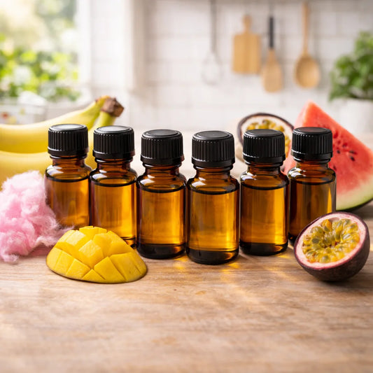 Set of small amber glass bottles with black caps on a wooden surface with fruit and kitchen items in the background.
