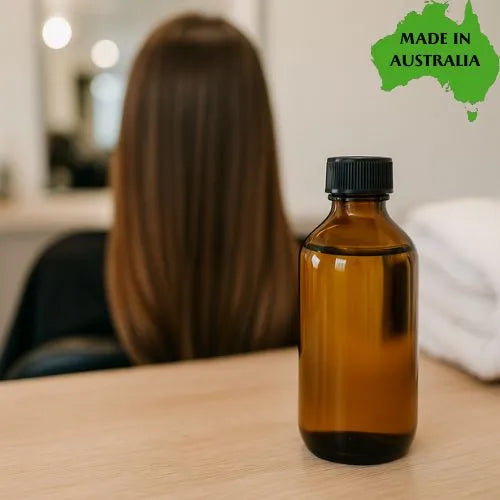 Brown bottle of Heirloom Hair Oil on a table with a blurred person and 'Made in Australia' label in the corner.