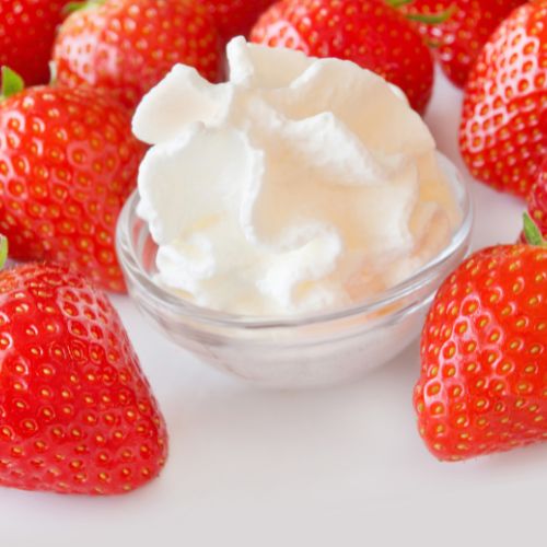 Strawberries gathered around a clear bowl of cream to represent Strawberries and Cream flavour oil